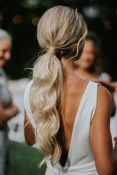 a woman with long blonde hair wearing a white dress and looking at another person in the background