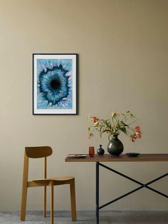 a table with two chairs and a vase on it in front of a wall mounted painting