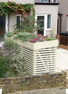 an outdoor garden with flowers and plants growing on the side of a building in front of a house