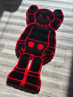 a black and red teddy bear rug sitting on top of a wooden floor next to a person's shadow