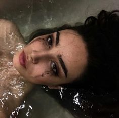 a woman laying in the bathtub with her eyes closed and water all over her face