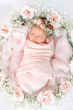 a newborn baby wrapped in a pink blanket surrounded by flowers