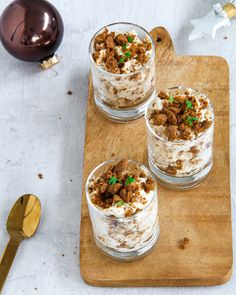 three glasses filled with dessert sitting on top of a wooden cutting board