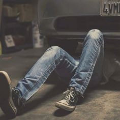 a man laying on the ground in front of a car with his feet propped up