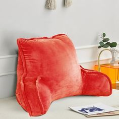 a red chair sitting on top of a white floor next to a wall with tassels hanging from it