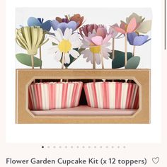 three cupcakes in a box with paper flowers on them and some sticks sticking out of the top