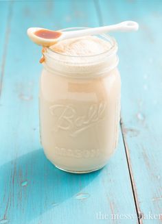 a glass jar with a spoon in it sitting on a blue wooden table next to a straw