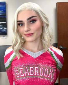 a woman with blonde hair and blue eyes wearing a pink shirt that says seabrook