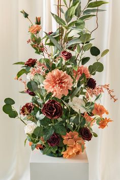 a vase filled with lots of flowers on top of a white table next to a curtain