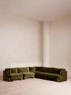 a large green couch sitting in the middle of a room next to a white wall