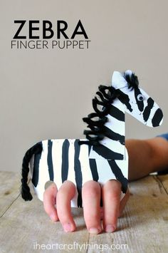 a zebra finger puppet sitting on top of a wooden table next to a child's hand