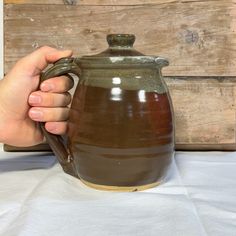 a hand holding a brown ceramic pitcher on top of a table