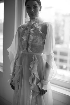 a woman standing in front of a window wearing a dress with ruffles on it