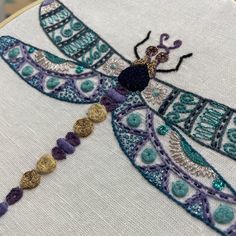 a close up of a dragonfly on a white cloth with gold and purple beads