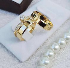 two gold wedding rings sitting on top of a white ring box next to some pearls