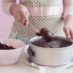 a woman stirring chocolate in a pot with a spoon and bowl next to it on a table