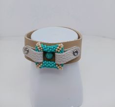 "This listing is for one handmade leather strap bracelet.  The center leather strap of the bracelet features a bead-woven square of seed beads in the colors of light turquoise and cream.  The square has a center of simulated turquoise, and a sparkling crystal on each side.  The bracelet is 1\" wide, and 8\" in length.  There is a magnetic snap closure." Adjustable Beaded Turquoise Leather Bracelet, Adjustable Turquoise Beaded Leather Bracelet, Handmade Adjustable Rectangular Leather Bracelet, Handmade Adjustable Square Beaded Bracelets, Unique Adjustable Beaded Leather Bracelet, Adjustable Square Turquoise Jewelry, Adjustable Beaded Leather Bracelet, Beaded Square, Light Turquoise