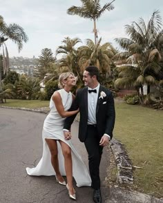 a man in a tuxedo and a woman in a white dress are walking down the street