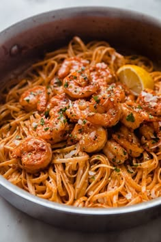 a bowl filled with pasta and shrimp on top of a table next to a lemon wedge