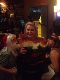 three women dressed up as santa clause and other people at a bar with drinks in their hands