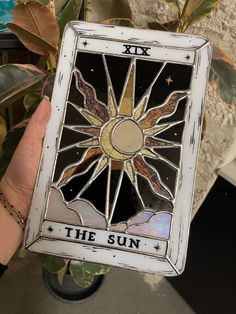 a person holding up a stained glass sun tarot in front of a potted plant