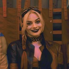 a woman with braids and leather jacket smiling at the camera while standing in front of wooden chairs