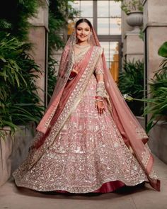 a woman in a pink and gold bridal gown posing for the camera with greenery behind her