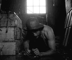 a shirtless man in a hat looking at his cell phone while sitting on the floor