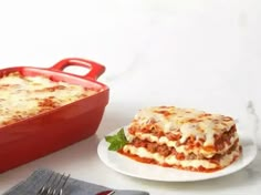 a red casserole dish with lasagna on it next to a white plate