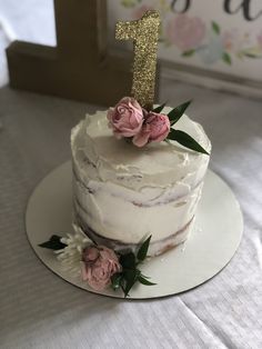 a white cake with pink flowers and a gold number one on top is sitting on a table