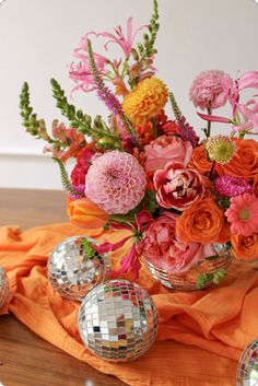 a vase filled with lots of flowers on top of a wooden table next to disco balls