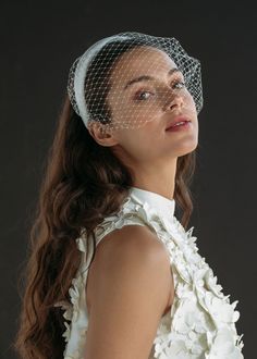 a woman wearing a birdcage veil with flowers on her head and dress underneath