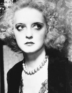 black and white photograph of a woman with blonde hair wearing pearls, necklaces and earrings