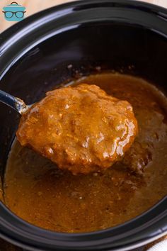 the meat is being cooked in the crock pot with sauce on it and a spoon