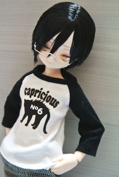 a doll with black hair and glasses wearing a white shirt that says capricious no 6