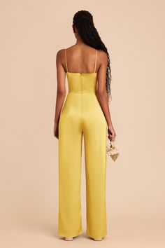 a woman in a yellow jumpsuit with her back turned to the camera, looking down