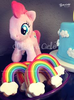 a pink pony sitting next to a rainbow cake and cupcakes on a plate