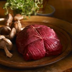 a piece of meat sitting on top of a wooden plate next to mushrooms