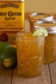 two jars filled with liquid sitting on top of a wooden table next to limes