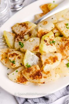 a white plate topped with potatoes covered in seasoning next to a fork and glass of water