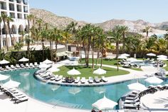 an aerial view of a resort pool with lounge chairs and umbrellas in the foreground