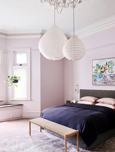 a bedroom with pink walls and two lamps hanging from the ceiling over the headboard