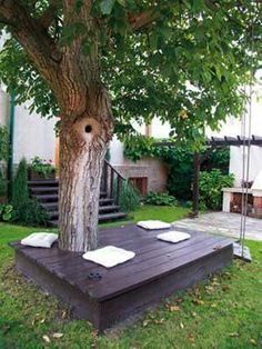 a tree in the middle of a yard with white pillows on it and stairs leading up to an upper level deck