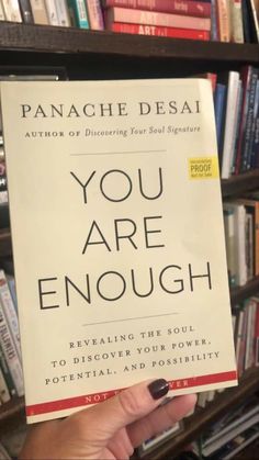 a person holding up a book with the title you are enough written on it in front of a bookshelf