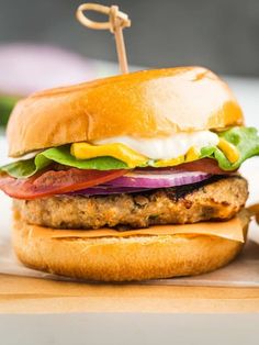 a hamburger with lettuce, tomato and cheese on it sitting on a cutting board