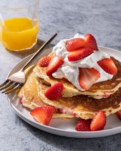 pancakes with whipped cream and strawberries on a plate next to a glass of orange juice