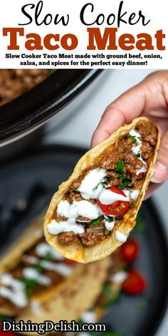 a hand holding up a taco with meat and sour cream on top, over a black plate