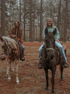 two girls are riding horses in the woods