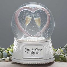 two champagne flutes in a heart shaped snow globe