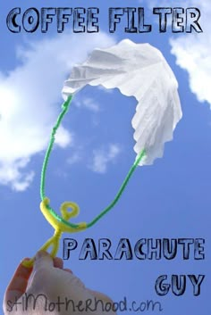 a hand holding a white paper flower with the words coffee filter parachute guy on it